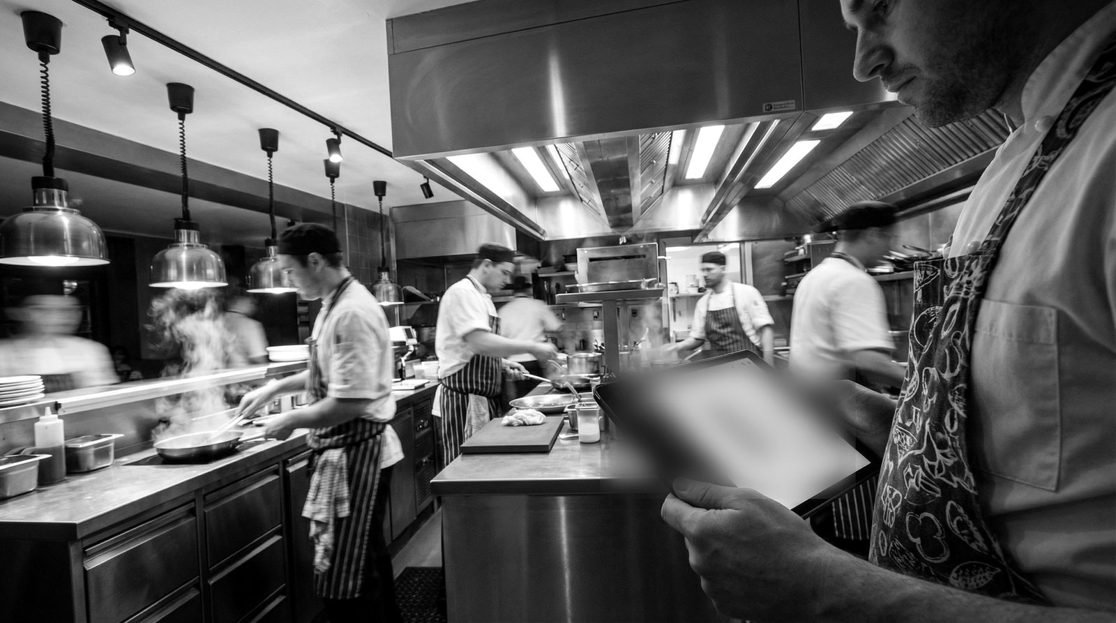 A kitchen team working a busy shift while a manager checks the schedule on a tablet